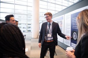 A Resident presents their poster to a group of colleagues at the interactive poster session